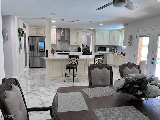 kitchen featuring stainless steel appliances, cream cabinets, pendant lighting, and wall chimney exhaust hood