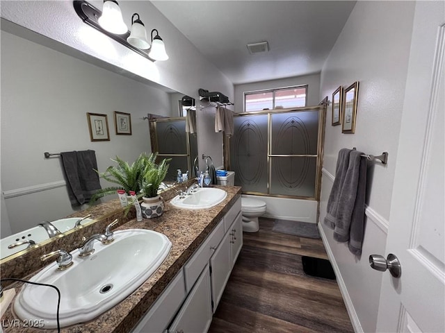 full bathroom with bath / shower combo with glass door, hardwood / wood-style floors, vanity, and toilet