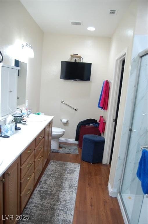 bathroom featuring wood-type flooring, toilet, vanity, and walk in shower