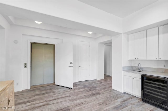 kitchen with sink, light hardwood / wood-style floors, beverage cooler, and white cabinets