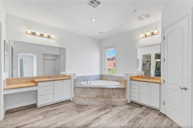 bathroom with hardwood / wood-style flooring, vanity, and a relaxing tiled tub