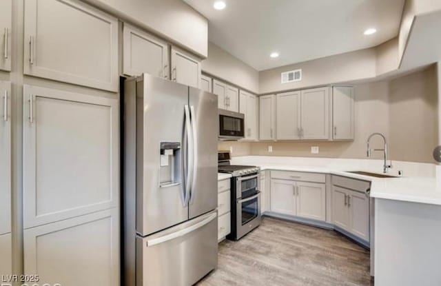 kitchen with appliances with stainless steel finishes, sink, gray cabinetry, and light wood-type flooring