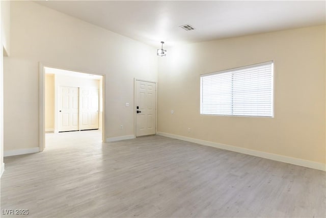 empty room featuring a towering ceiling and light hardwood / wood-style flooring