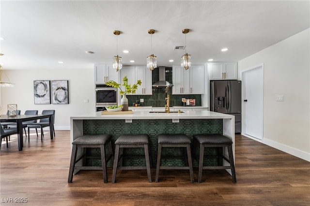 kitchen with white cabinetry, wall chimney exhaust hood, fridge with ice dispenser, and hanging light fixtures