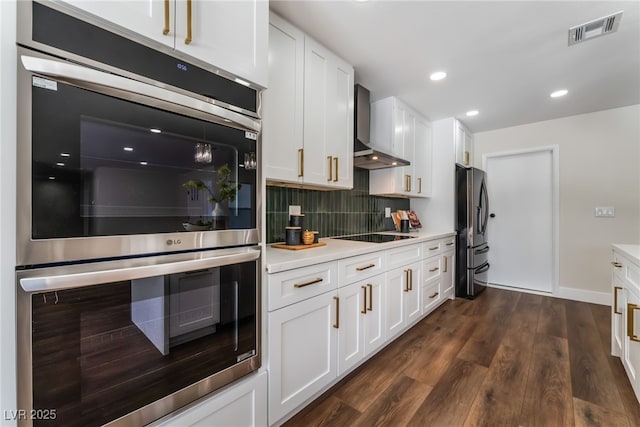 kitchen with double oven, refrigerator with ice dispenser, backsplash, white cabinets, and wall chimney exhaust hood