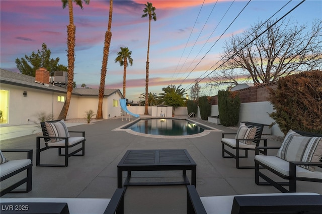 pool at dusk featuring a patio area, an outdoor hangout area, and a water slide