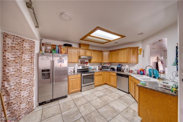 kitchen with appliances with stainless steel finishes, sink, dark stone counters, and light tile patterned floors