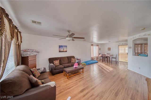 living room featuring ceiling fan, a textured ceiling, and light wood-type flooring