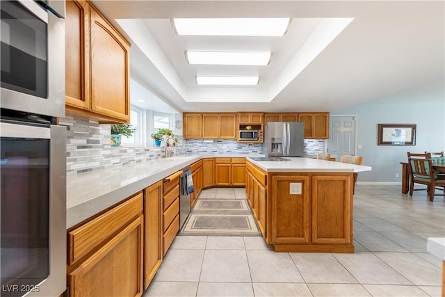 kitchen featuring light tile patterned flooring, a kitchen island, appliances with stainless steel finishes, decorative backsplash, and a raised ceiling