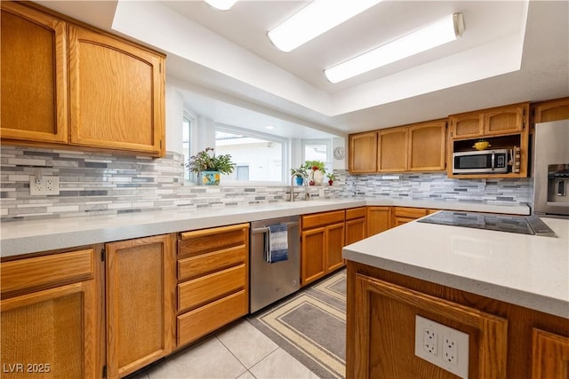 kitchen with light tile patterned flooring, appliances with stainless steel finishes, tasteful backsplash, sink, and a tray ceiling