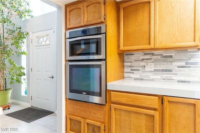 kitchen with double oven, backsplash, plenty of natural light, and light tile patterned flooring