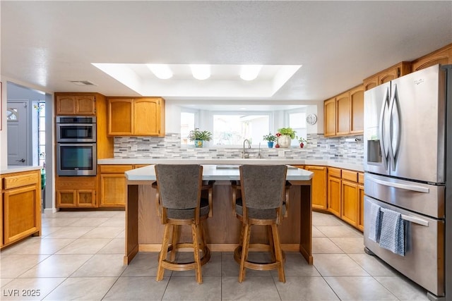 kitchen featuring appliances with stainless steel finishes, a kitchen breakfast bar, a raised ceiling, and a kitchen island