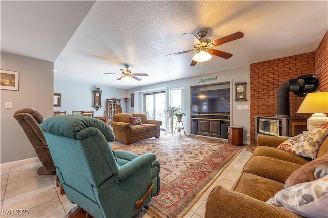 living room with ceiling fan, a wood stove, light tile patterned floors, and a textured ceiling