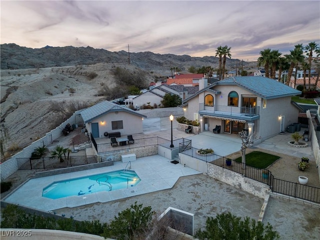 back house at dusk featuring a fenced in pool, a balcony, a mountain view, and a patio area