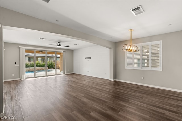 empty room with ceiling fan with notable chandelier and dark hardwood / wood-style flooring