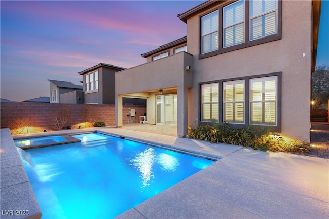 pool at dusk with an in ground hot tub, pool water feature, and a patio area