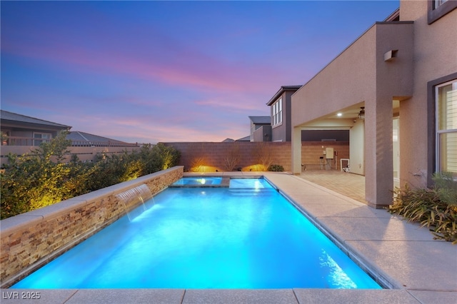 pool at dusk featuring pool water feature and a patio