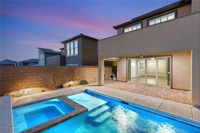 pool at dusk featuring a patio and an in ground hot tub