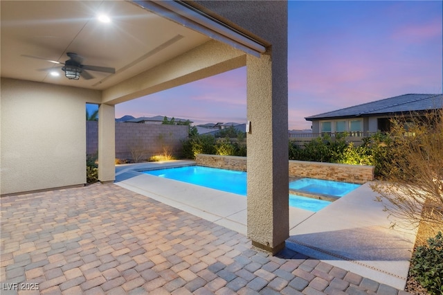 pool at dusk with a hot tub, ceiling fan, and a patio area