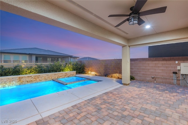 pool at dusk featuring a patio area, ceiling fan, and a jacuzzi