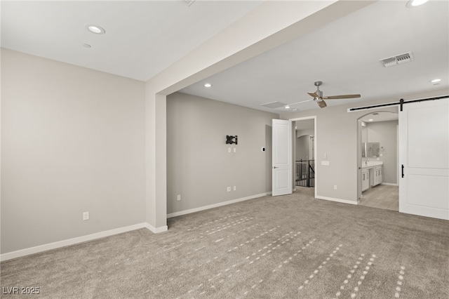 unfurnished bedroom with a walk in closet, a barn door, light carpet, and ensuite bath