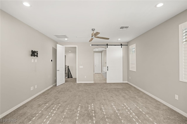 unfurnished bedroom featuring light colored carpet, a barn door, and ceiling fan