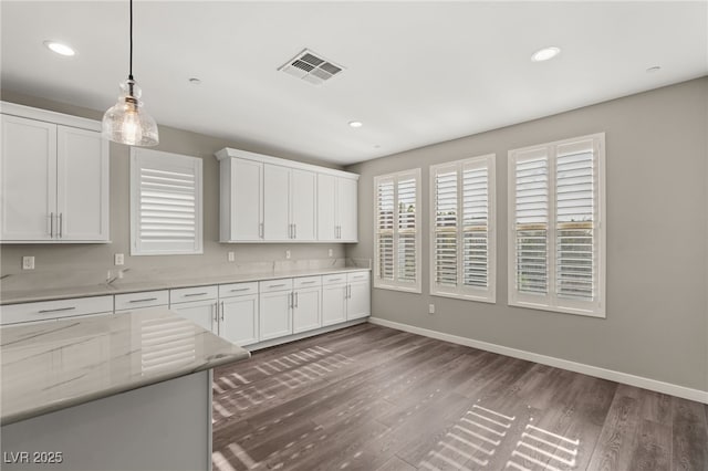 kitchen with hanging light fixtures, dark wood-type flooring, light stone countertops, and white cabinets