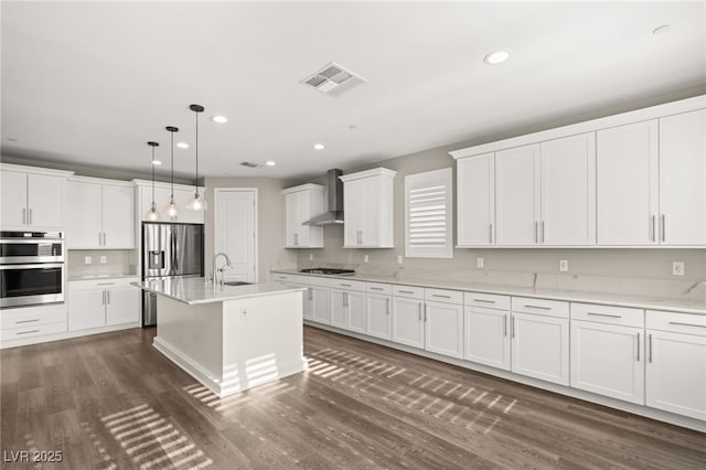 kitchen with pendant lighting, sink, stainless steel appliances, an island with sink, and wall chimney exhaust hood