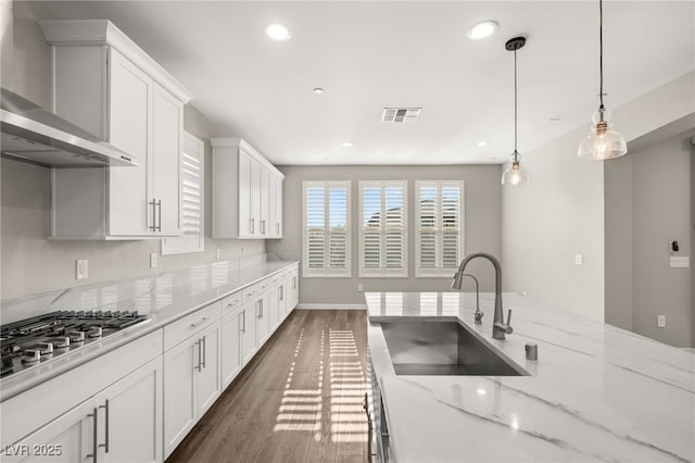 kitchen with sink, white cabinetry, hanging light fixtures, wall chimney exhaust hood, and stainless steel gas stovetop