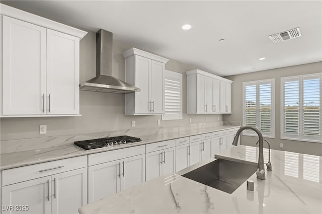 kitchen with stainless steel gas stovetop, white cabinetry, sink, light stone countertops, and wall chimney range hood