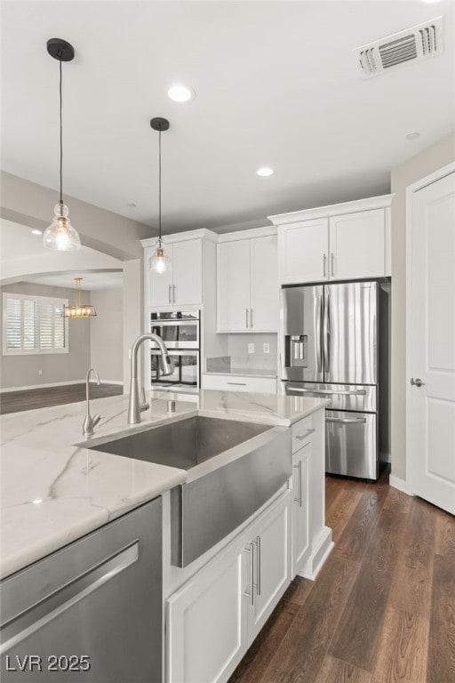 kitchen with decorative light fixtures, white cabinetry, sink, light stone counters, and stainless steel appliances