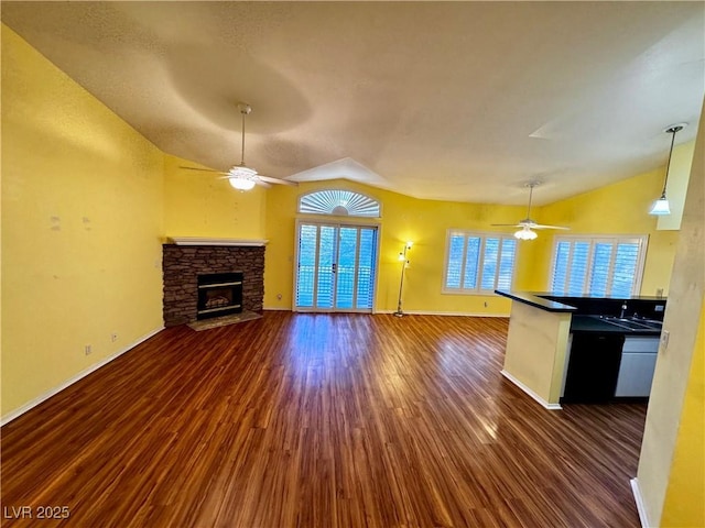 unfurnished living room with lofted ceiling, a ceiling fan, dark wood-style flooring, and a stone fireplace