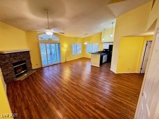 unfurnished living room with lofted ceiling, a stone fireplace, dark wood-style flooring, a ceiling fan, and baseboards