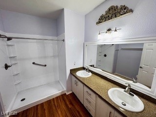 full bathroom featuring double vanity, wood finished floors, walk in shower, and a sink