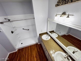 bathroom with a sink, double vanity, walk in shower, and wood finished floors