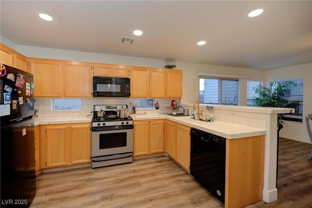 kitchen with sink, tile counters, light brown cabinets, and black appliances