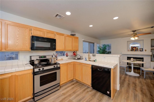 kitchen with tile countertops, black appliances, light hardwood / wood-style floors, and light brown cabinets