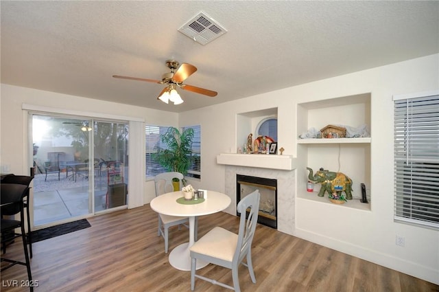 dining area featuring hardwood / wood-style flooring, ceiling fan, a textured ceiling, and a high end fireplace