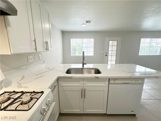 kitchen with a textured ceiling, a peninsula, white appliances, a sink, and wall chimney range hood