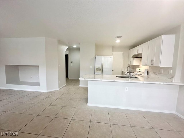 kitchen featuring under cabinet range hood, a peninsula, white appliances, a sink, and baseboards