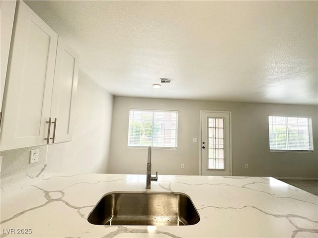 kitchen with light stone counters, a sink, visible vents, and white cabinetry