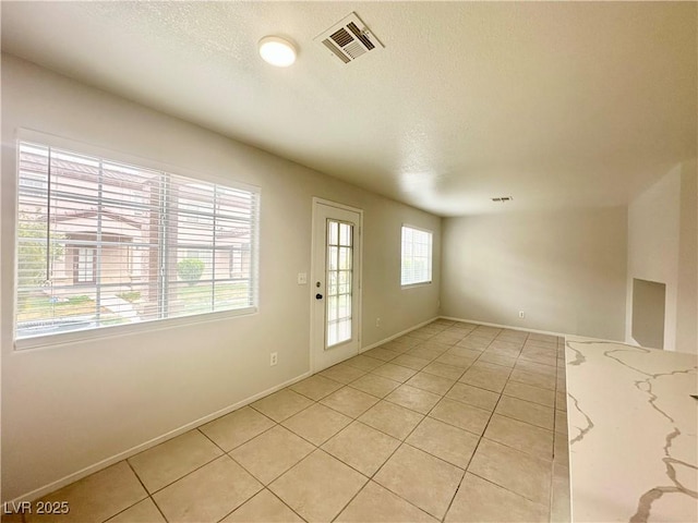 unfurnished room featuring visible vents, a textured ceiling, and light tile patterned flooring