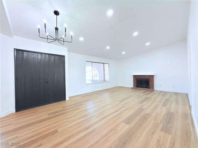 unfurnished living room with vaulted ceiling, a brick fireplace, a notable chandelier, and light wood-type flooring