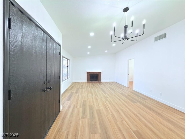 unfurnished living room with a notable chandelier, a brick fireplace, and light wood-type flooring