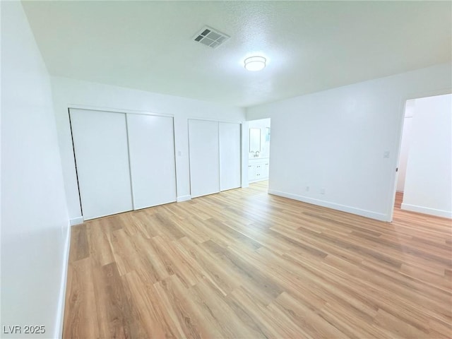 unfurnished bedroom featuring light hardwood / wood-style flooring and multiple closets