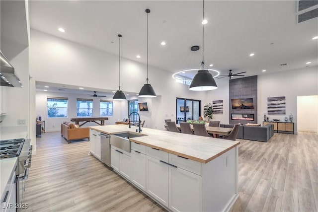 kitchen with sink, appliances with stainless steel finishes, white cabinetry, hanging light fixtures, and butcher block counters