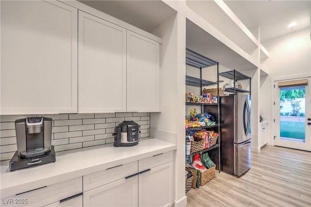 kitchen with white cabinetry, decorative backsplash, stainless steel refrigerator, and light hardwood / wood-style flooring