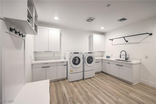 washroom with washer and dryer, sink, light hardwood / wood-style floors, and cabinets