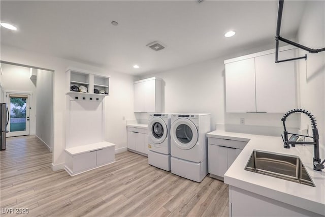 laundry area featuring separate washer and dryer, sink, cabinets, and light wood-type flooring