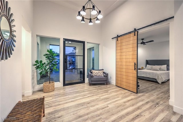 foyer with an inviting chandelier, a towering ceiling, a barn door, and light hardwood / wood-style flooring